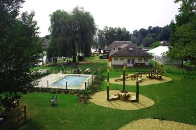 Aire de jeux en bois sur un sol sablé, entourée de verdure et située près d'une rivière et de collines.