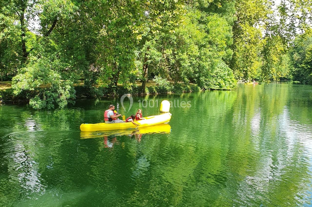 Deux personnes pagayant dans un canoë jaune sur une rivière bordée d'arbres verdoyants.