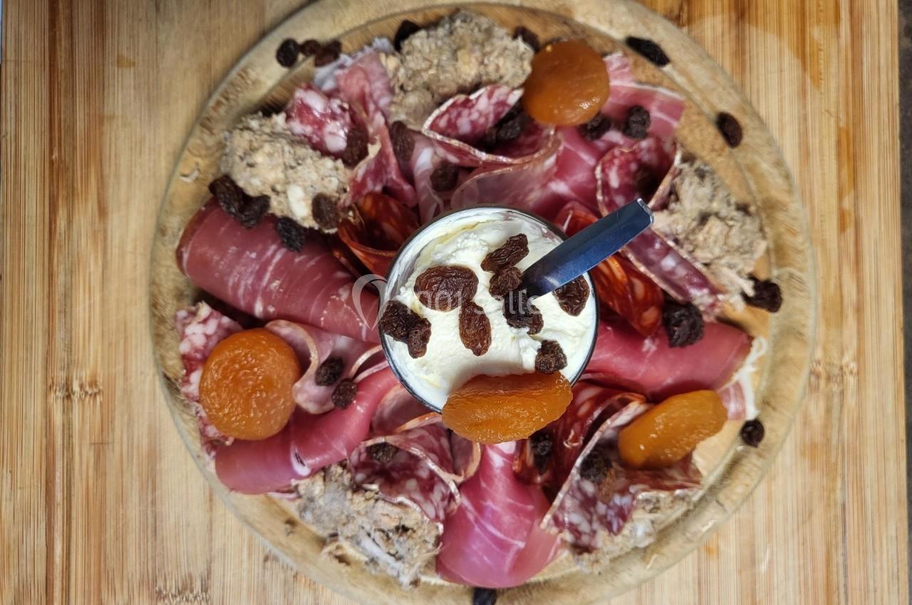 Plateau de charcuterie avec jambon, saucisson, fruits secs et une verrine de crème garnie de raisins secs.