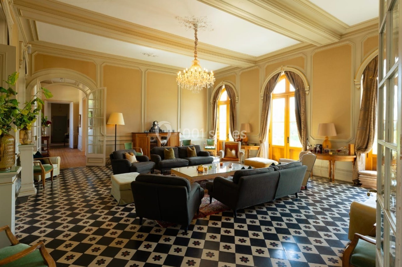 Salon spacieux avec parquet en damier noir et blanc, mobilier élégant et lustre central, baigné de lumière naturelle.