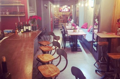 Intérieur d'un bar cosy avec un comptoir en bois, des tabourets hauts et des tables alignées dans un espace chaleureux.