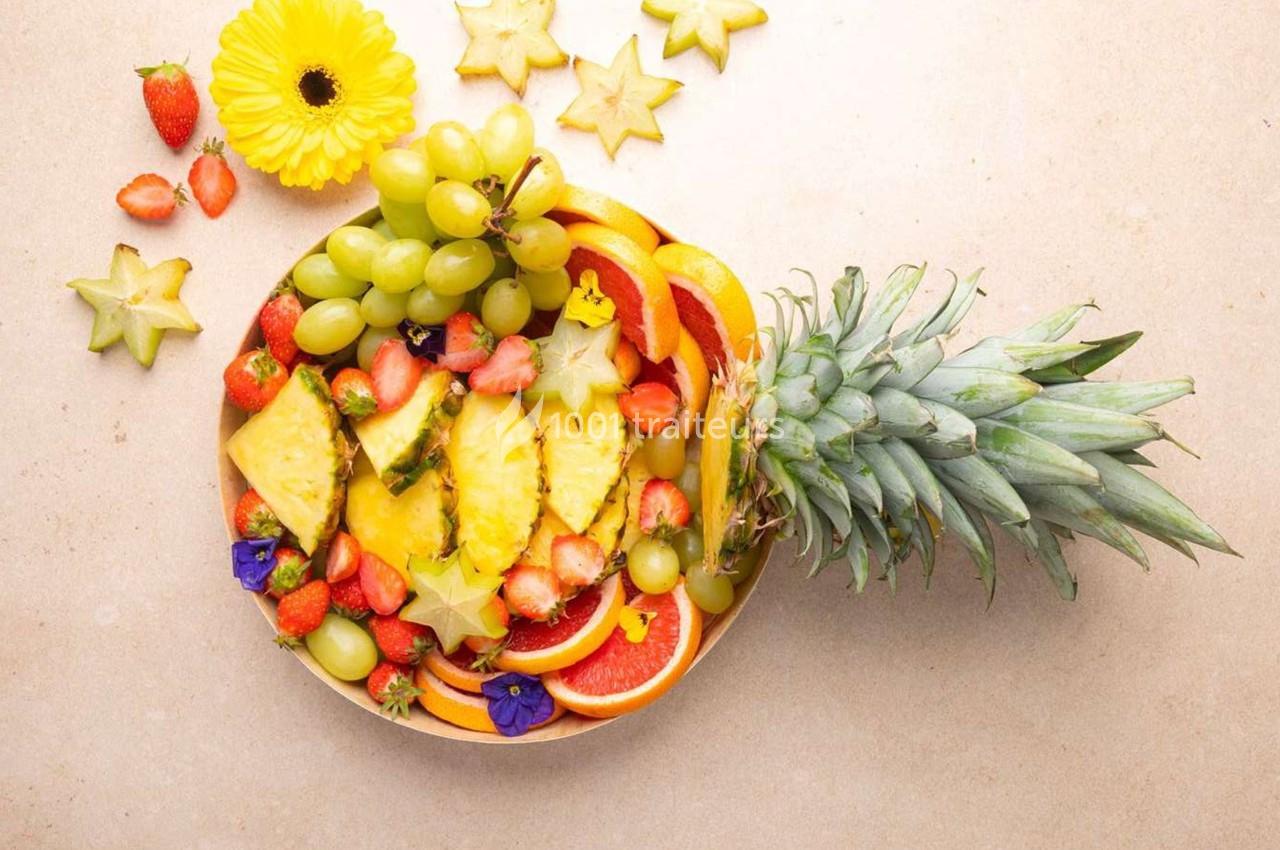 Assortiment de fruits frais comprenant ananas, fraises, raisins, oranges, caramboles et fleurs comestibles sur une table…