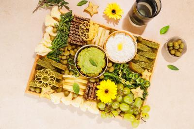 Plateau coloré de crudités, fromages, dips, fruits secs et fleurs comestibles disposés de manière artistique.