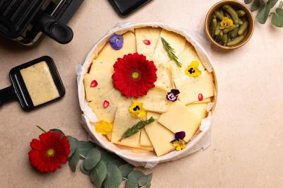 Plateau coloré de crudités, fromages, dips, fruits secs et fleurs comestibles disposés de manière artistique.