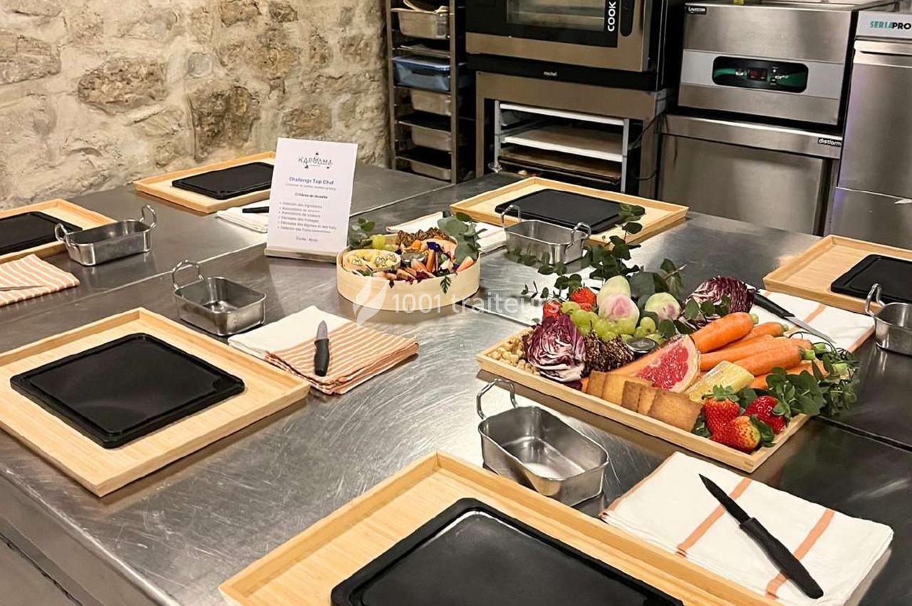 Plan de travail en cuisine avec planches en bois, assiettes noires, légumes frais, fruits et ustensiles disposés pour un…