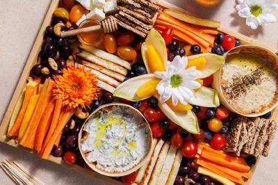 Plateau coloré de crudités, fromages, dips, fruits secs et fleurs comestibles disposés de manière artistique.