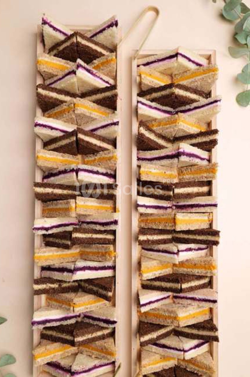 Deux plateaux en bois allongés chargés de petits sandwiches triangulaires, alignés en rangées serrées, avec des garnitures jaune orangé, violet et crème sur pain blanc et pain complet.