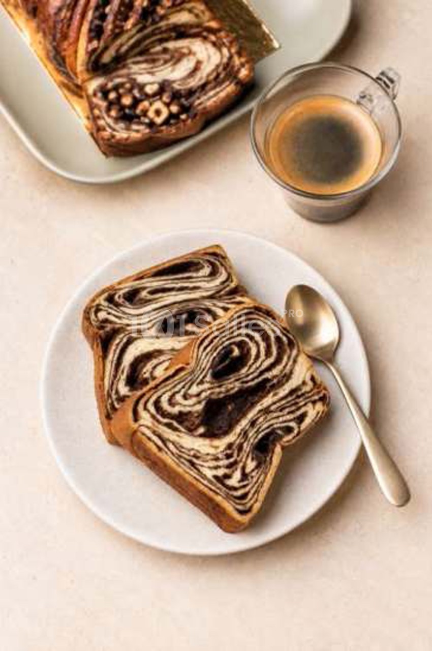 Deux tranches de brioche marbrée au chocolat sur une assiette blanche, près d'une tasse de café et d'une cuillère.