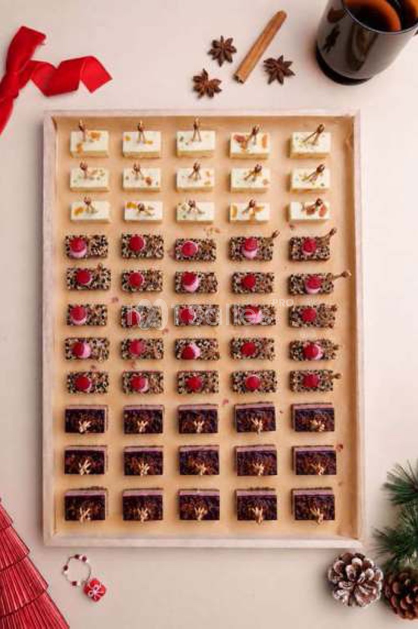 Plateau de petits fours sucrés alignés en rangées, crème blanche, glaçage chocolat et garniture rouge, décor de Noël.