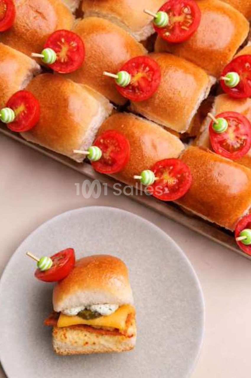 Plateau de mini-sandwichs briochés garnis de fromage fondu et de sauce, décorés de tomates cerises sur pique, et un sandwich servi seul sur une assiette grise. Let me check length: about 160 characters, too long. Need ≤125. Shorter: "Mini-sandwichs