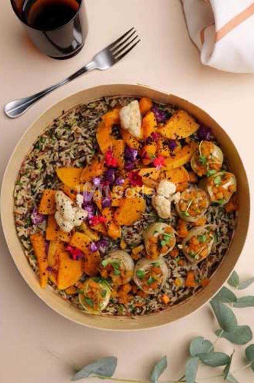 Plat végétarien dressé dans un plat rond en carton : riz sauvage, morceaux de courge rôtie, chou-fleur, petits farcis et fleurs comestibles, vu du dessus.
