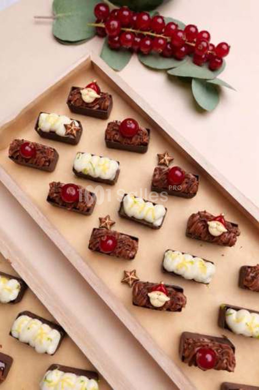 Plateau de petites bûches au chocolat décorées de baies rouges, de crème blanche zestée et d'étoiles dorées, disposées en rangées sur du papier kraft.