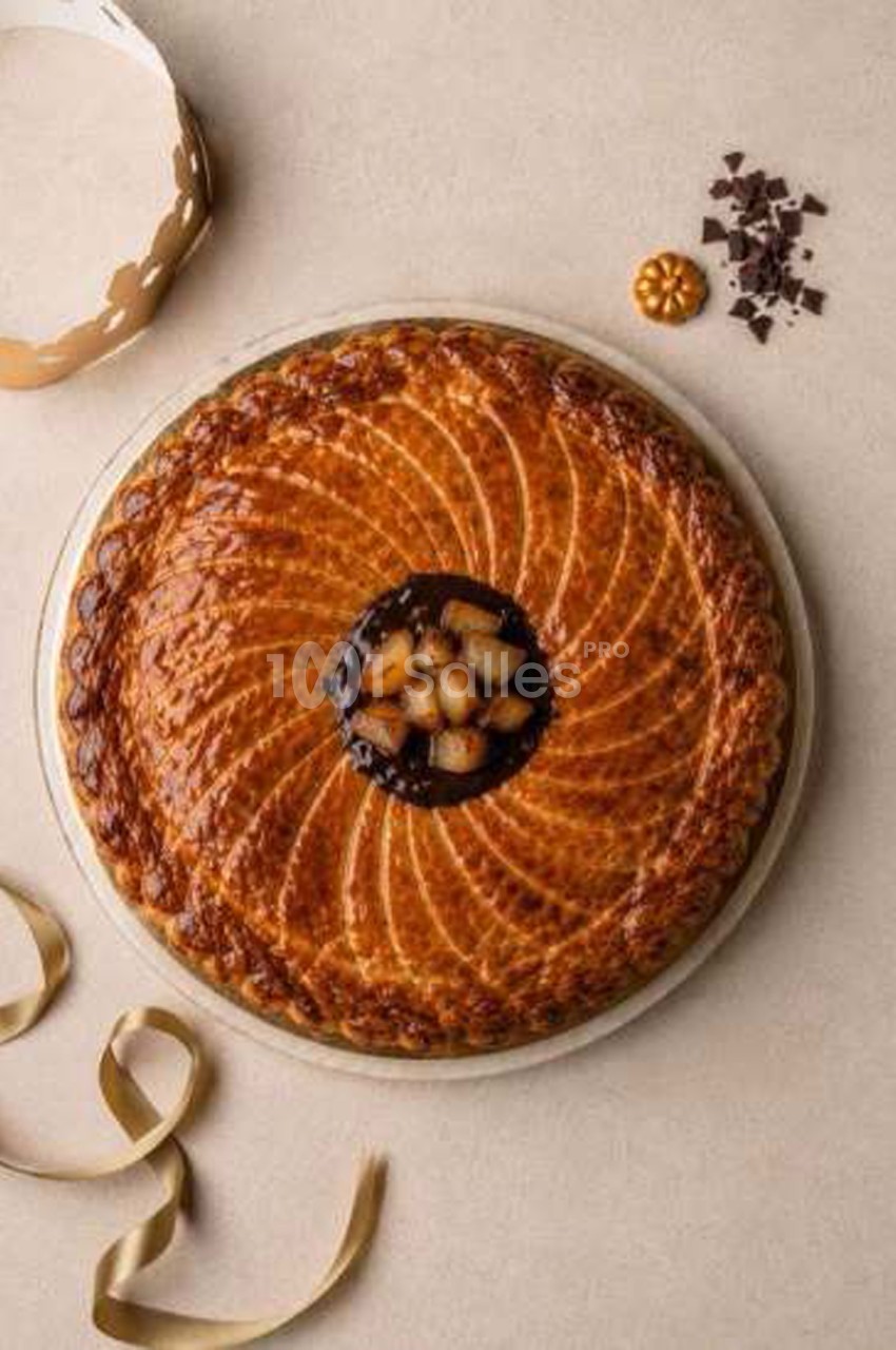 Galette des rois dorée à motif spiralé, garnie au centre de morceaux de poire et d'une crème sombre, posée sur un plateau, avec des copeaux de chocolat et des rubans dorés. Vérification : environ 190 caractères, trop long. Reformulation : Galette des