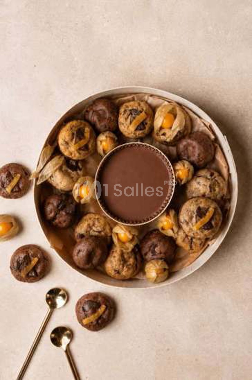 Plateau rond en carton beige garni de petits gâteaux au chocolat et à l'orange confite, avec un pot de crème au chocolat au centre, sur fond clair.