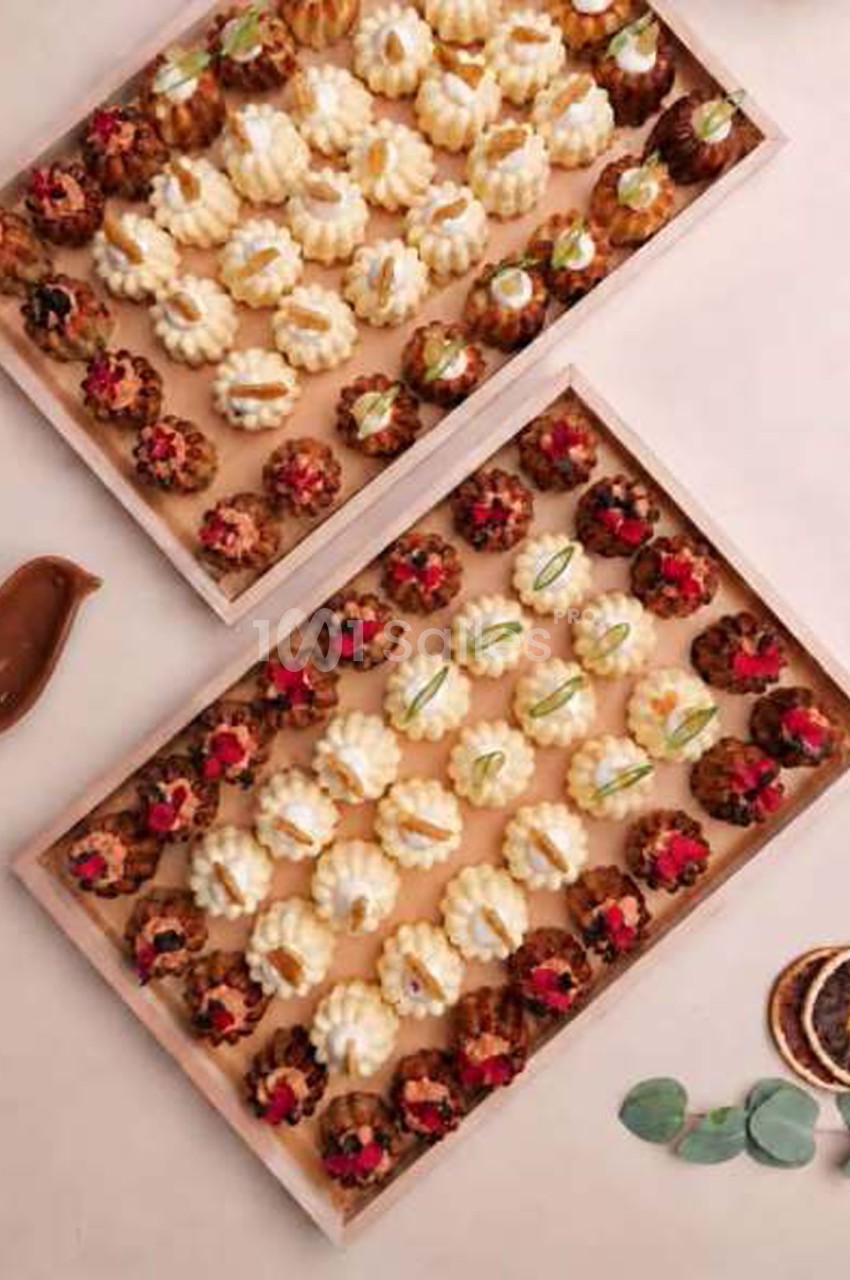 Deux plateaux en bois de petites pâtisseries cannelées : bruns garnis de pétales rouges, blancs ornés de lamelles dorées.