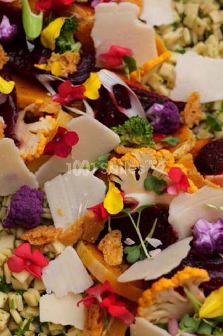 Assiette de salade composée de légumes colorés (betterave, carotte, chou-fleur violet), copeaux de fromage blanc, fleurs comestibles rouges et jaunes et céréales.