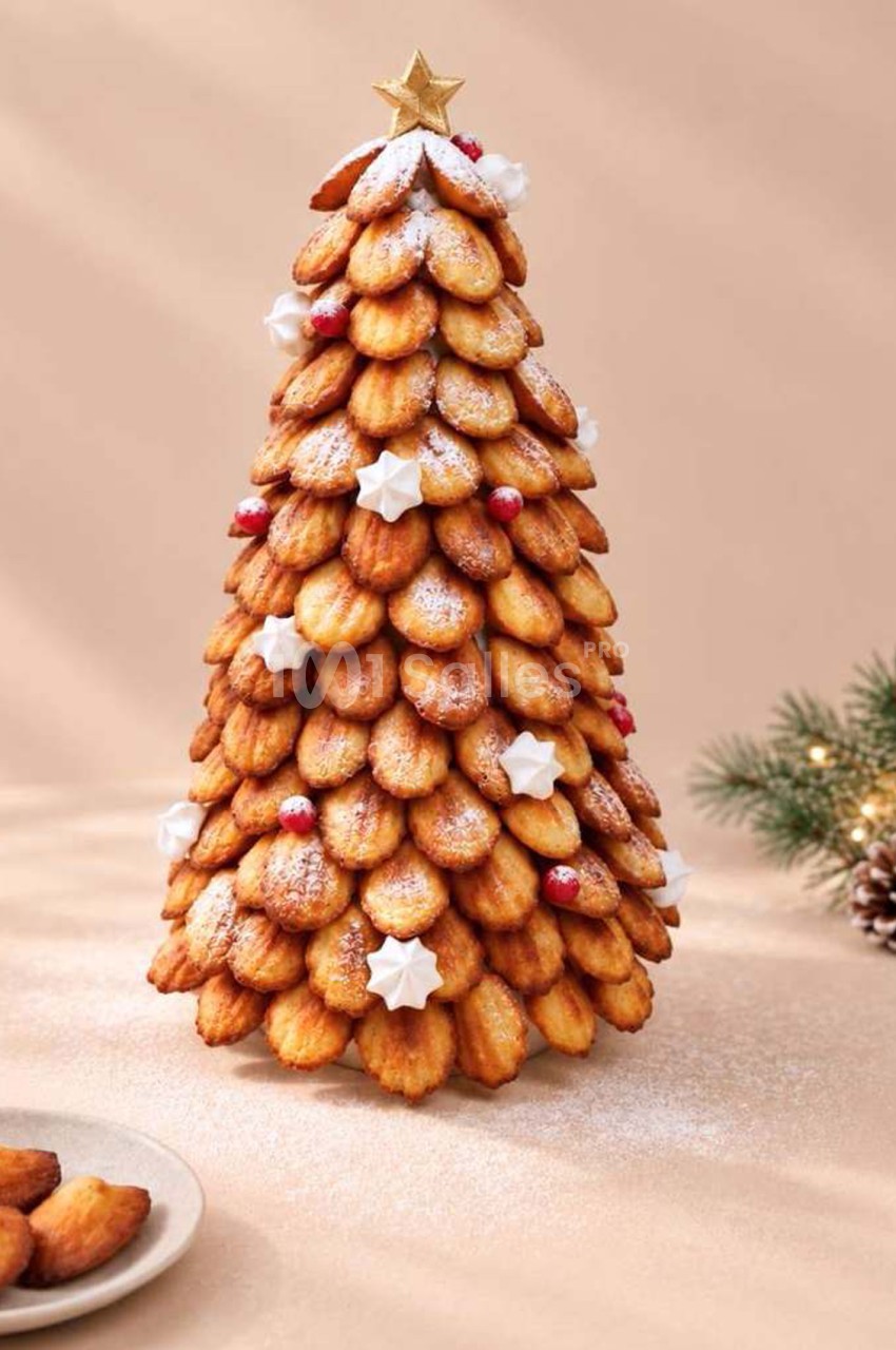 Sapin de Noël en madeleines dorées, saupoudrées de sucre glace, orné d'une étoile dorée au sommet et de meringues et baies rouges, posé sur un fond beige.