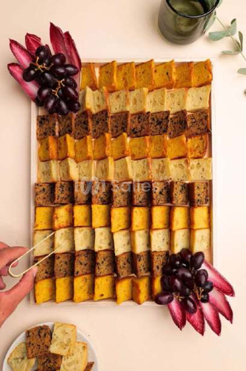 Plateau de cubes de cakes multicolores disposés en rangées, garni de raisin et de feuilles de chicorée rouge.