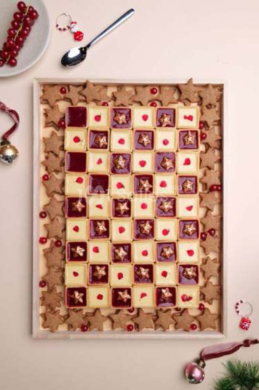 Plateau rectangulaire de petits sablés carrés en damier alternant pâte crème et confiture rouge foncée ornée d'une étoile dorée, entouré de biscuits étoilés et de groseilles.