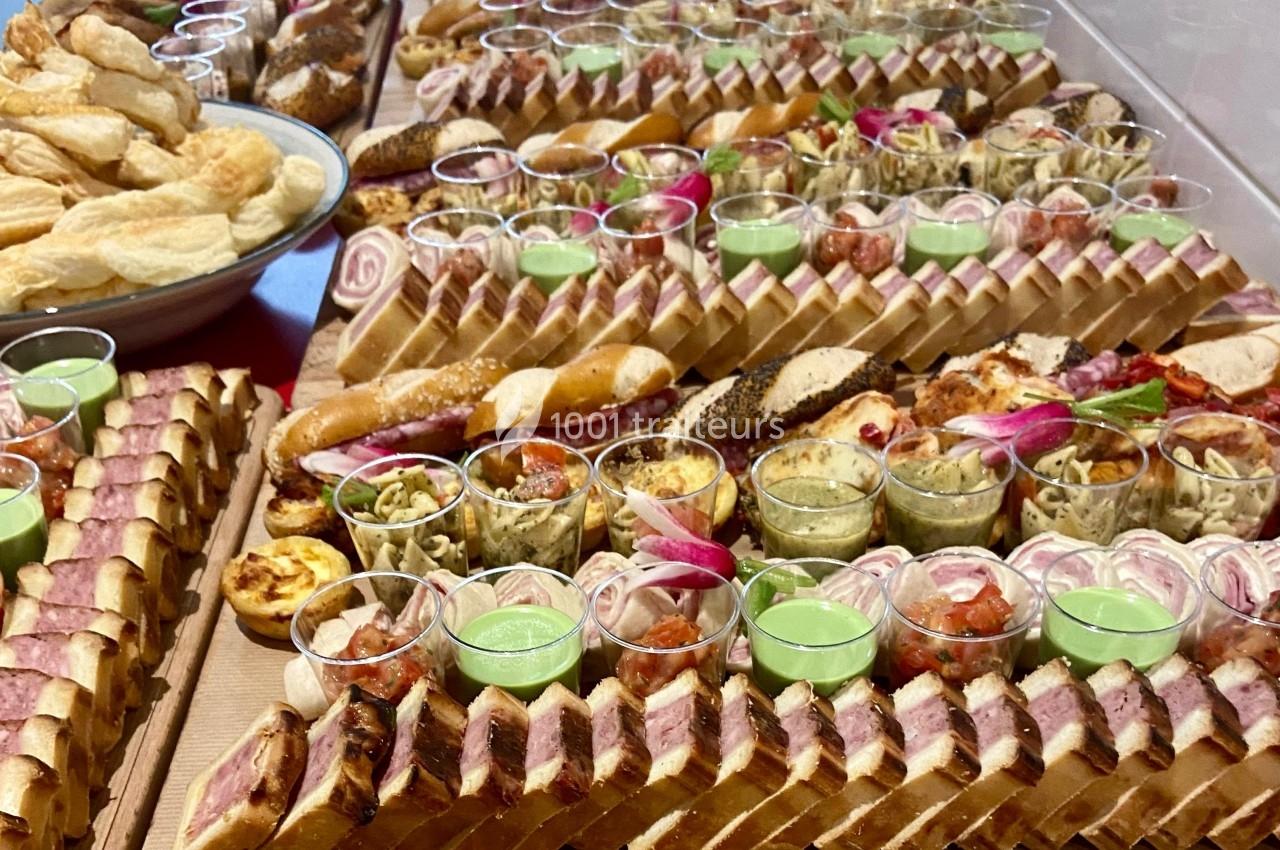 Plateau de buffet avec assortiments de sandwichs, verrines, quiches et feuilletés disposés en rangées.
