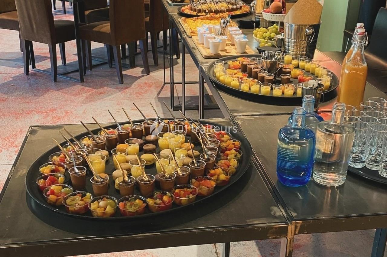 Buffet avec verrines de desserts, fruits frais et boissons disposés sur des tables dans une salle de réception.