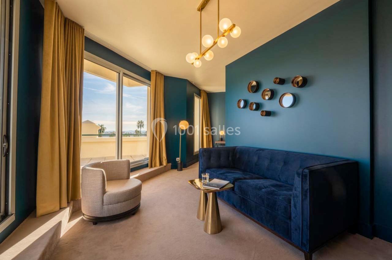 Location salle Hyères (Var) - Pasino de Hyères #11 Salon moderne avec canapé bleu, fauteuil beige, table dorée et grandes fenêtres offrant une vue sur l'extérieur.