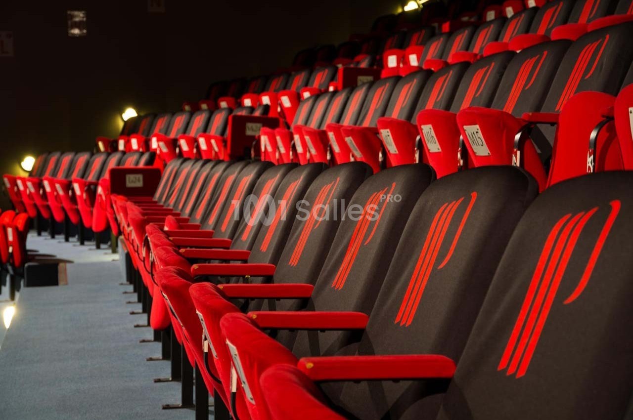 Rangées de fauteuils rouges alignés dans une salle de spectacle ou de cinéma, éclairage tamisé.
