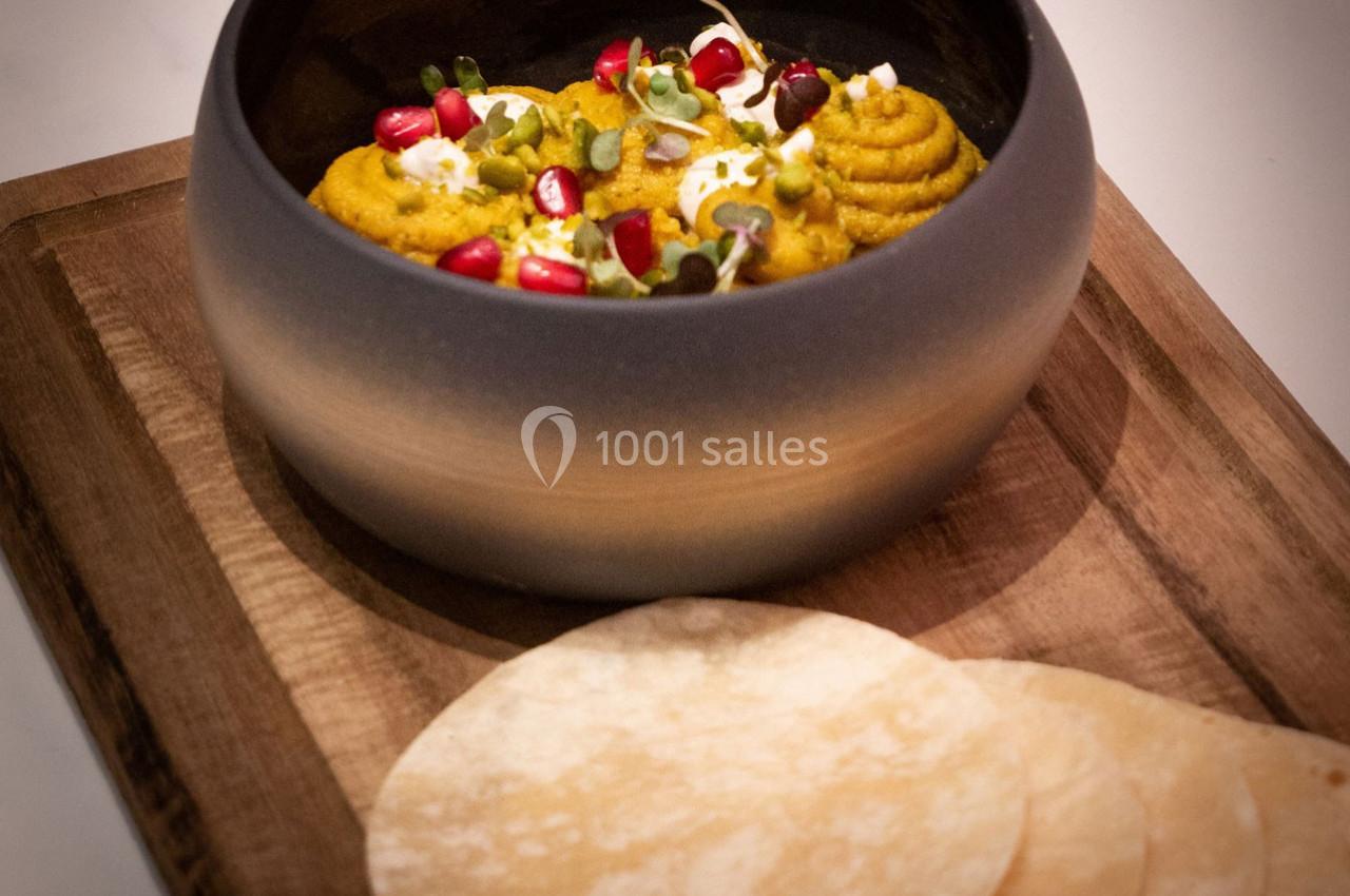 Location salle Hyères (Var) - Pasino de Hyères #9 Bol de purée garnie de graines de grenade et herbes fraîches, accompagné de galettes sur une planche en bois.