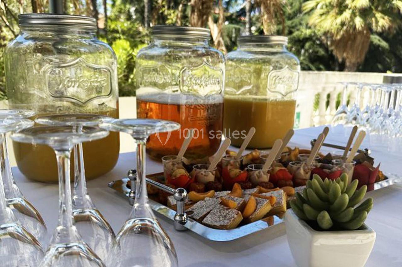 Location salle Hyères (Var) - Pasino de Hyères #14 Buffet extérieur avec boissons en jarres, verrines sucrées et salées, verres vides et plante décorative.