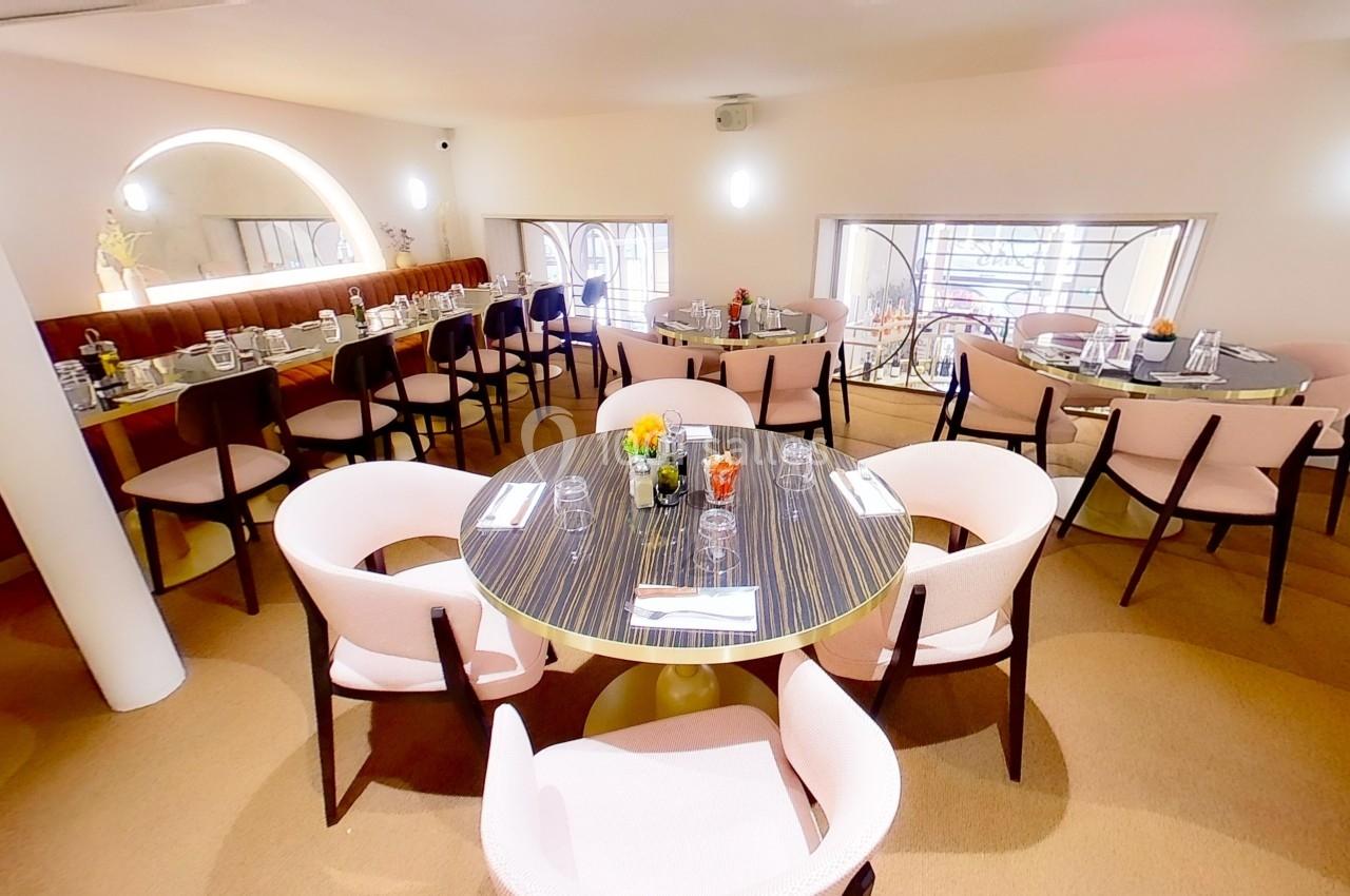 Salle de restaurant lumineuse avec des tables rondes dressées, entourées de chaises roses et un décor épuré.