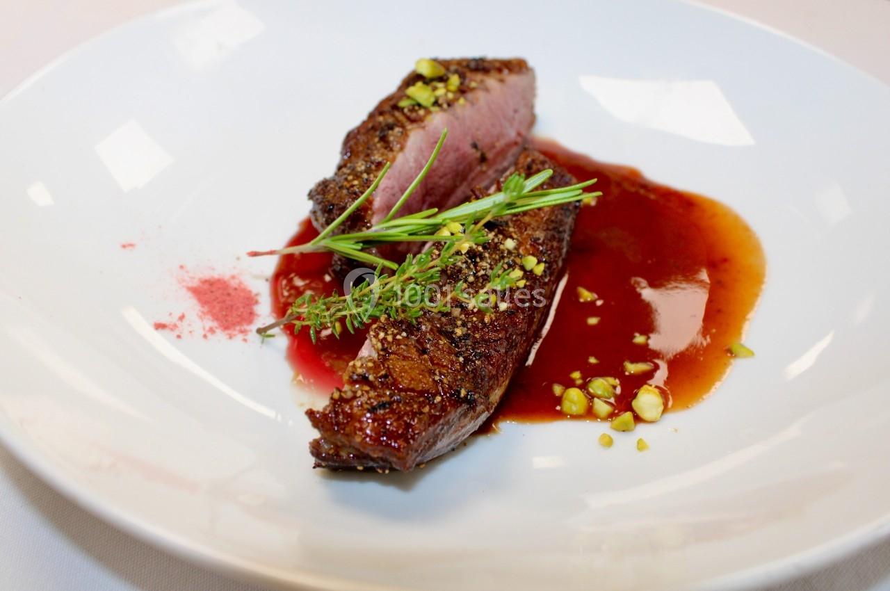 Tranche de viande cuite à point, nappée de sauce rouge, garnie d'herbes fraîches et de pistaches concassées.
