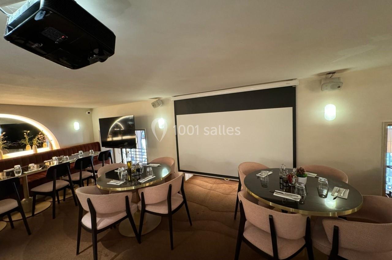 Salle de réunion avec tables rondes dressées, écran de projection et éclairage tamisé.