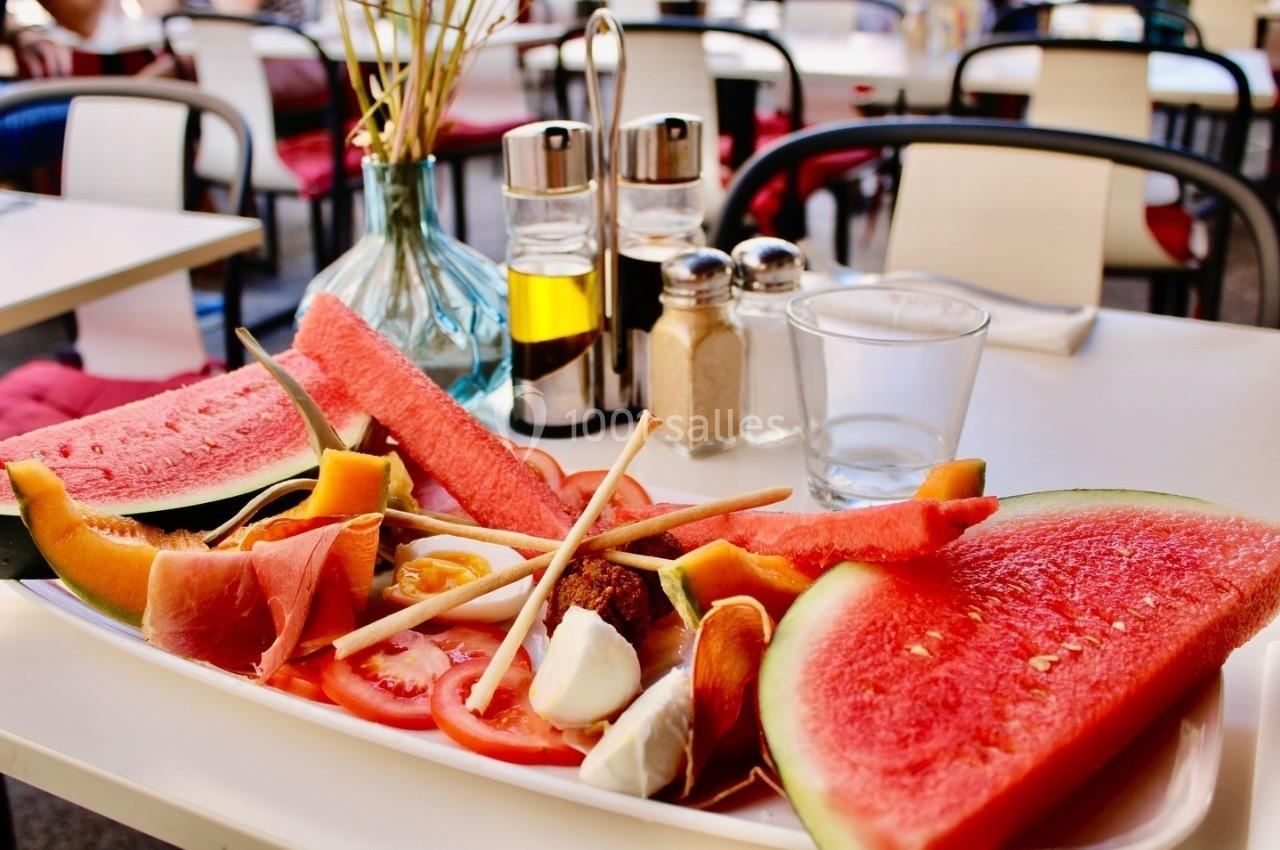 Assiette garnie de fruits frais, légumes, charcuterie et fromage, posée sur une table en terrasse.