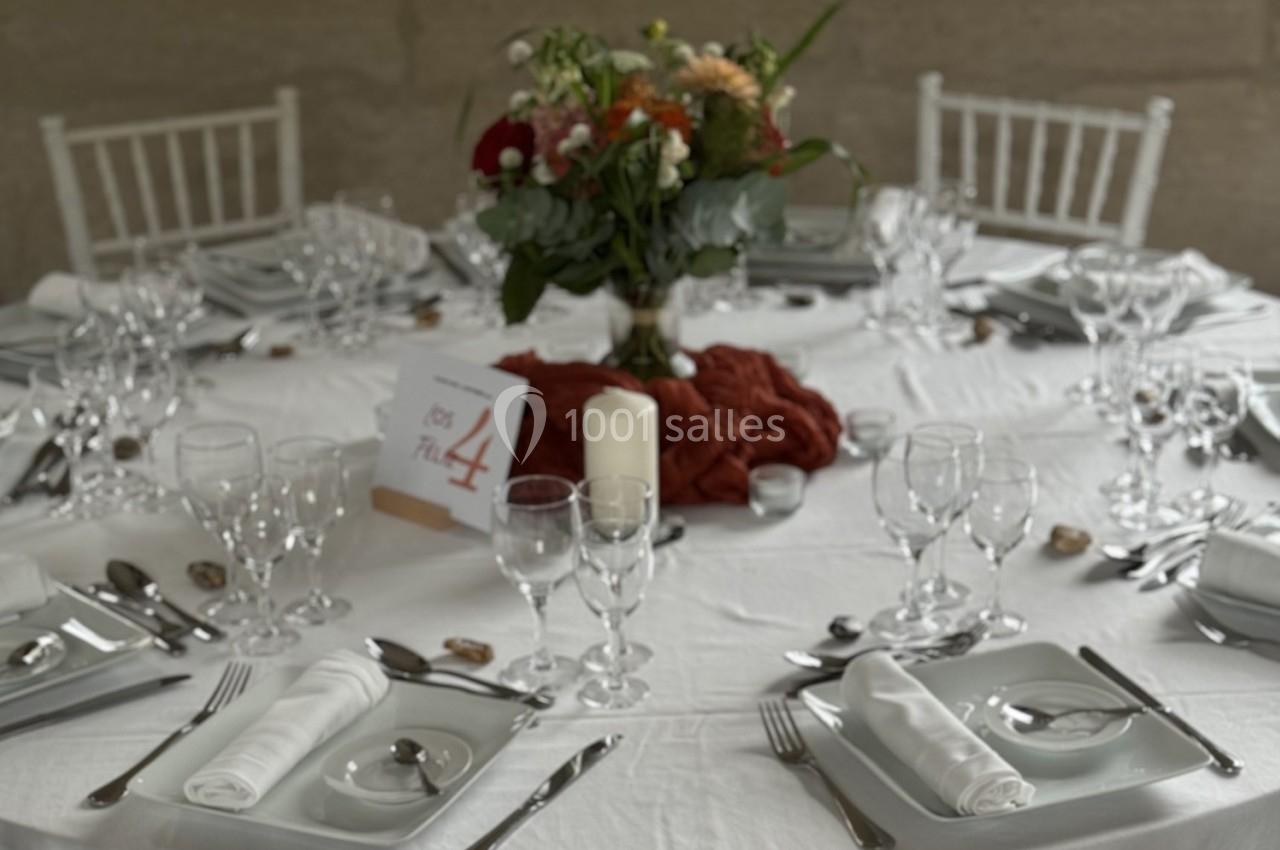 Table ronde élégamment dressée avec nappes blanches, vaisselle raffinée, centre de table floral et numéro 4.