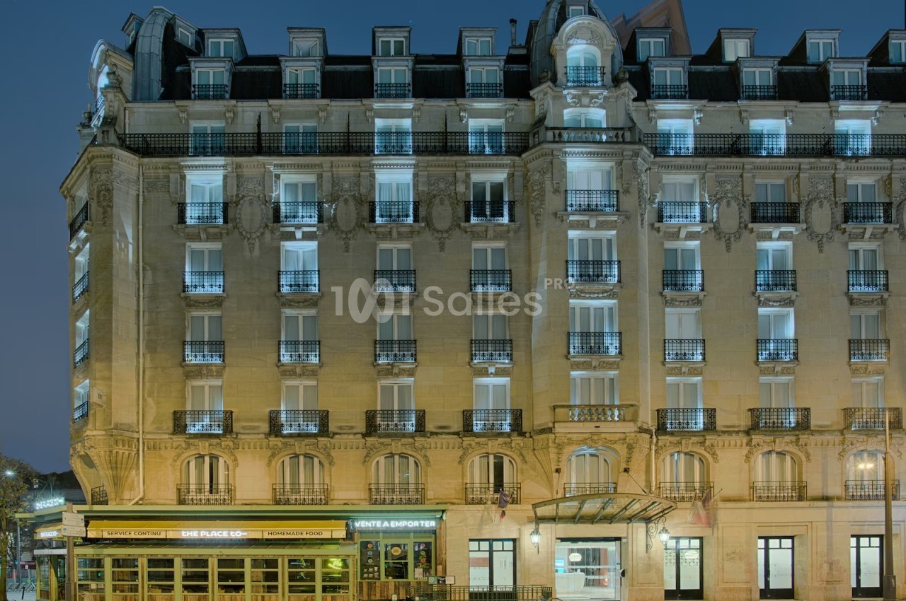 Façade d'un immeuble haussmannien éclairé de nuit, avec un restaurant et une entrée d'hôtel au rez-de-chaussée.