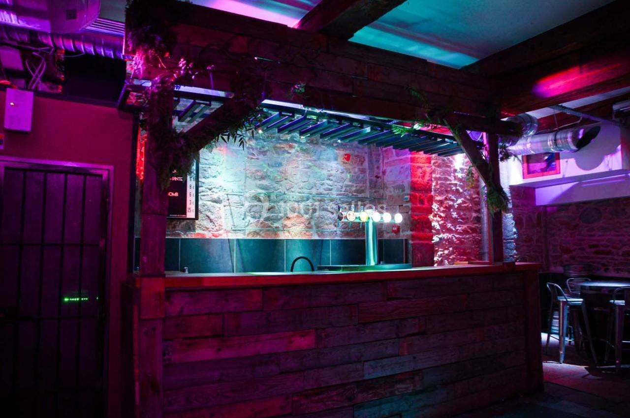 Bar en bois avec éclairage coloré dans un espace intérieur aux murs en pierre apparente.