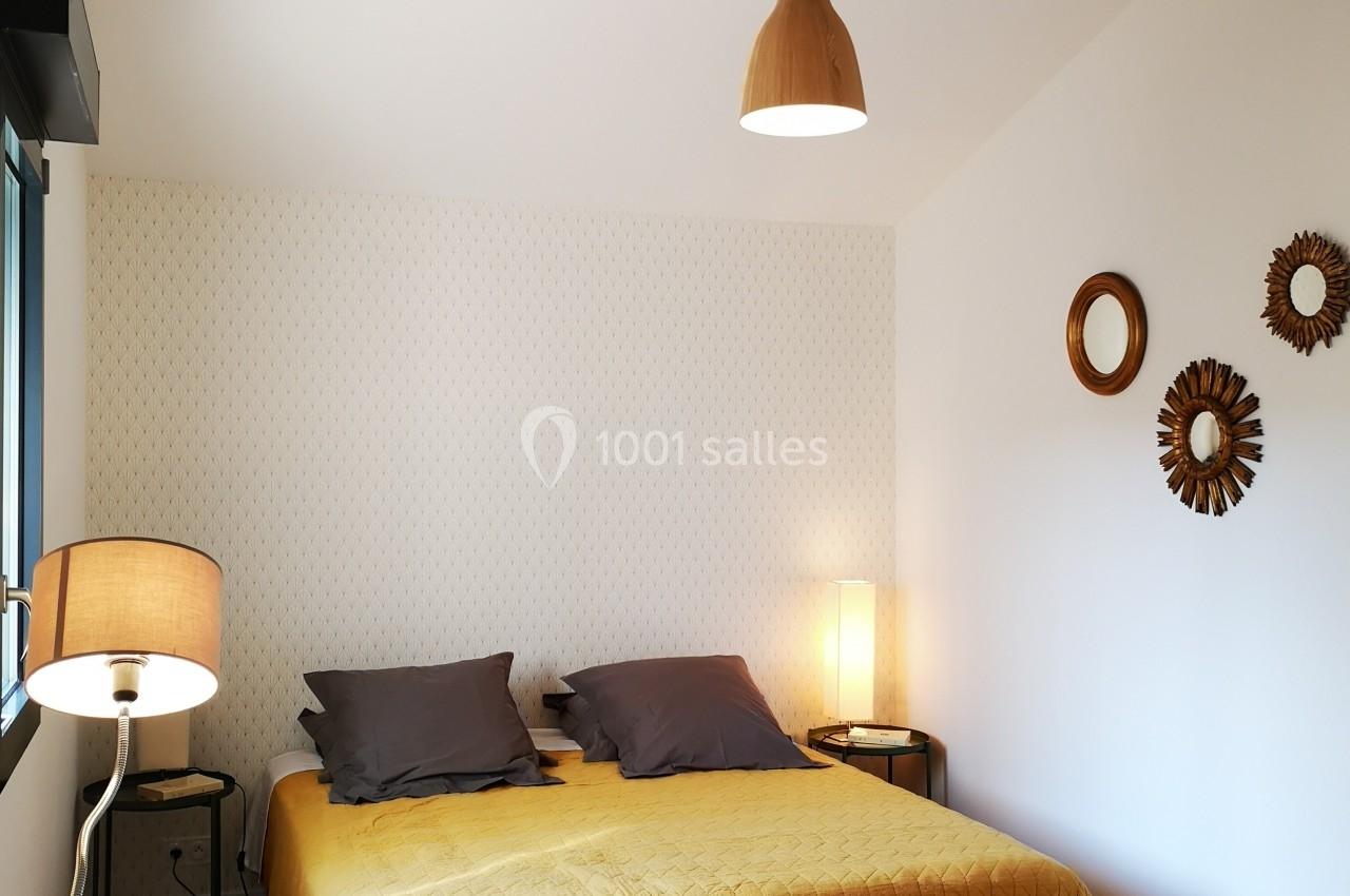 Chambre lumineuse avec un lit double à couverture jaune, lampes modernes et décoration murale en bois.