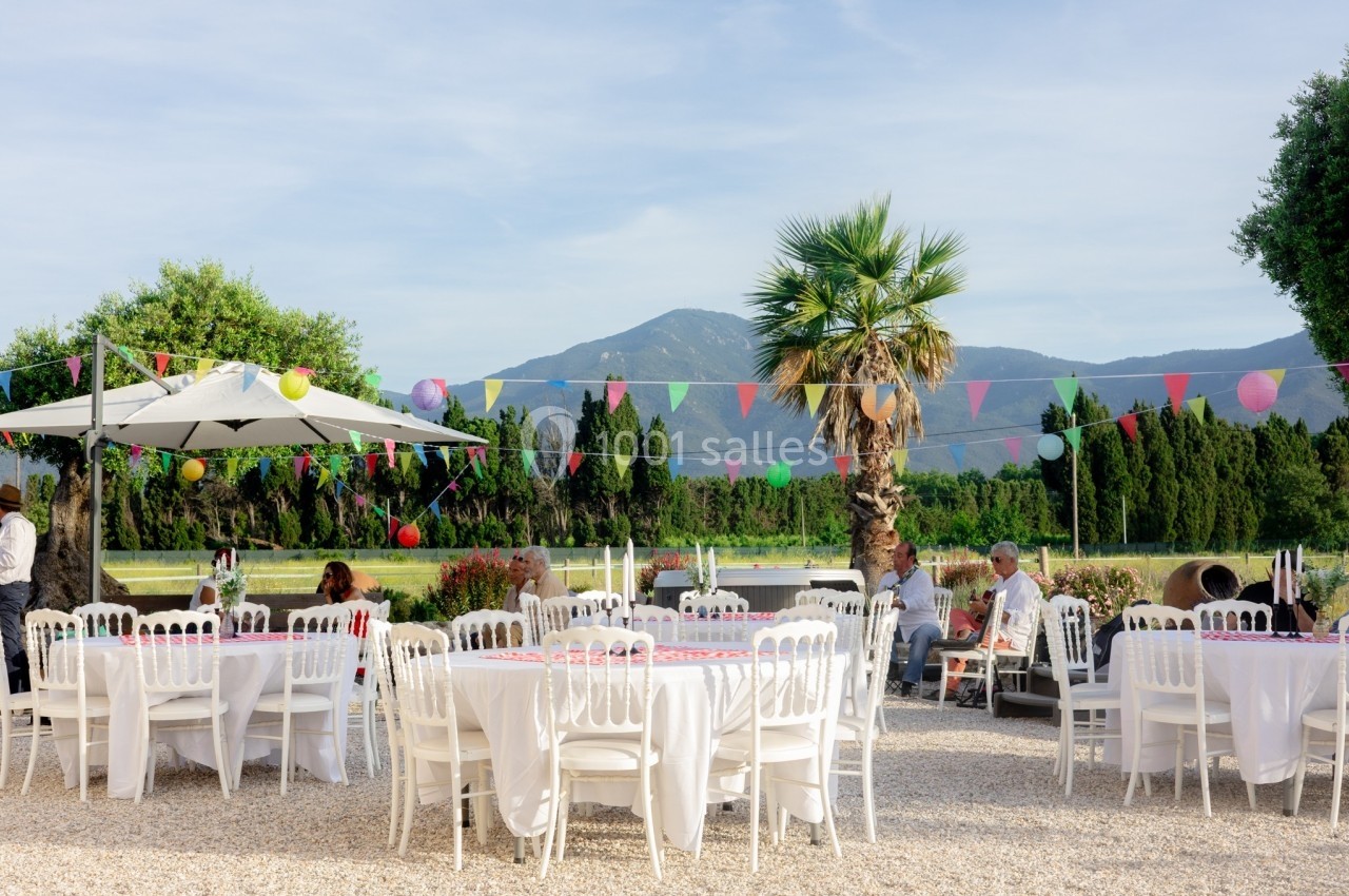 Tables blanches décorées pour un événement en plein air, avec guirlandes colorées et vue sur des montagnes.
