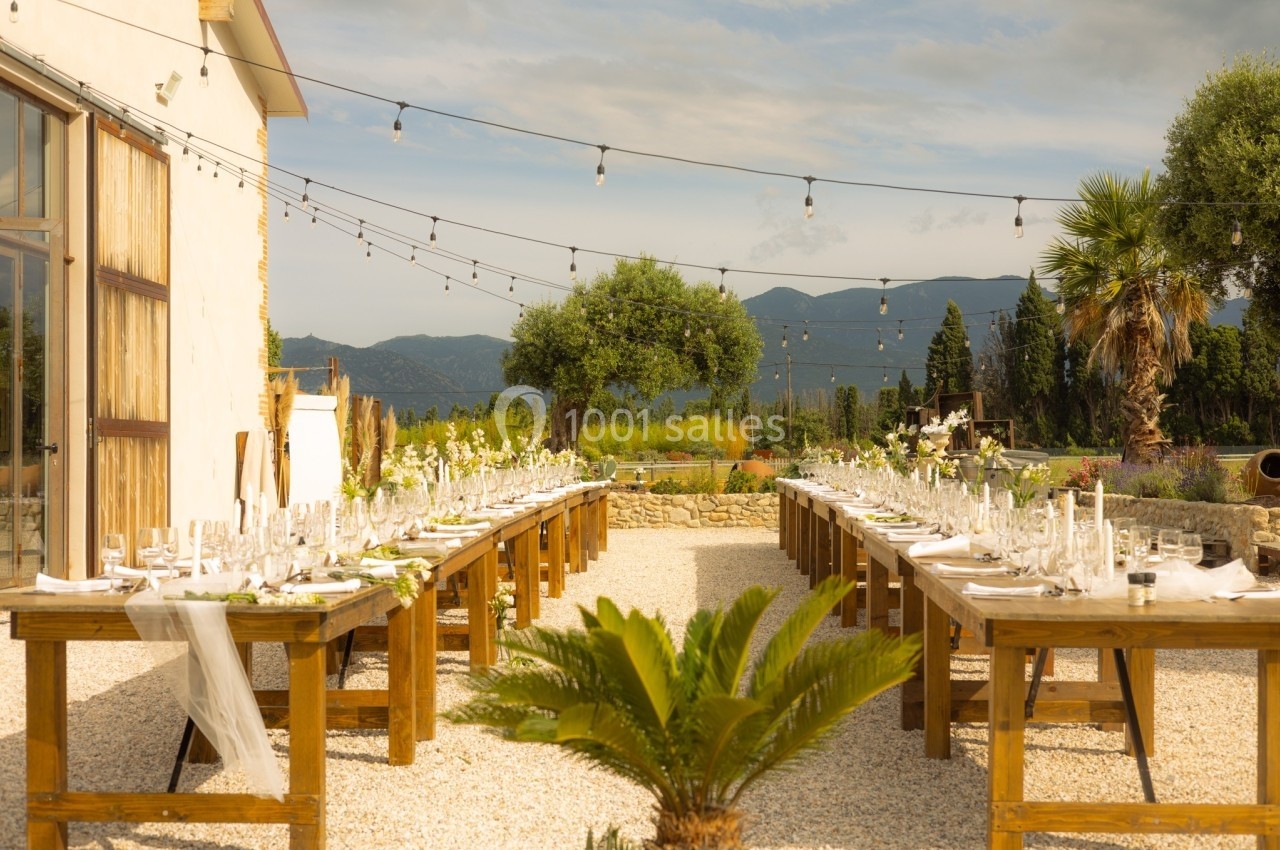 Tables en bois décorées pour un repas en extérieur, avec guirlandes lumineuses et vue sur des montagnes.