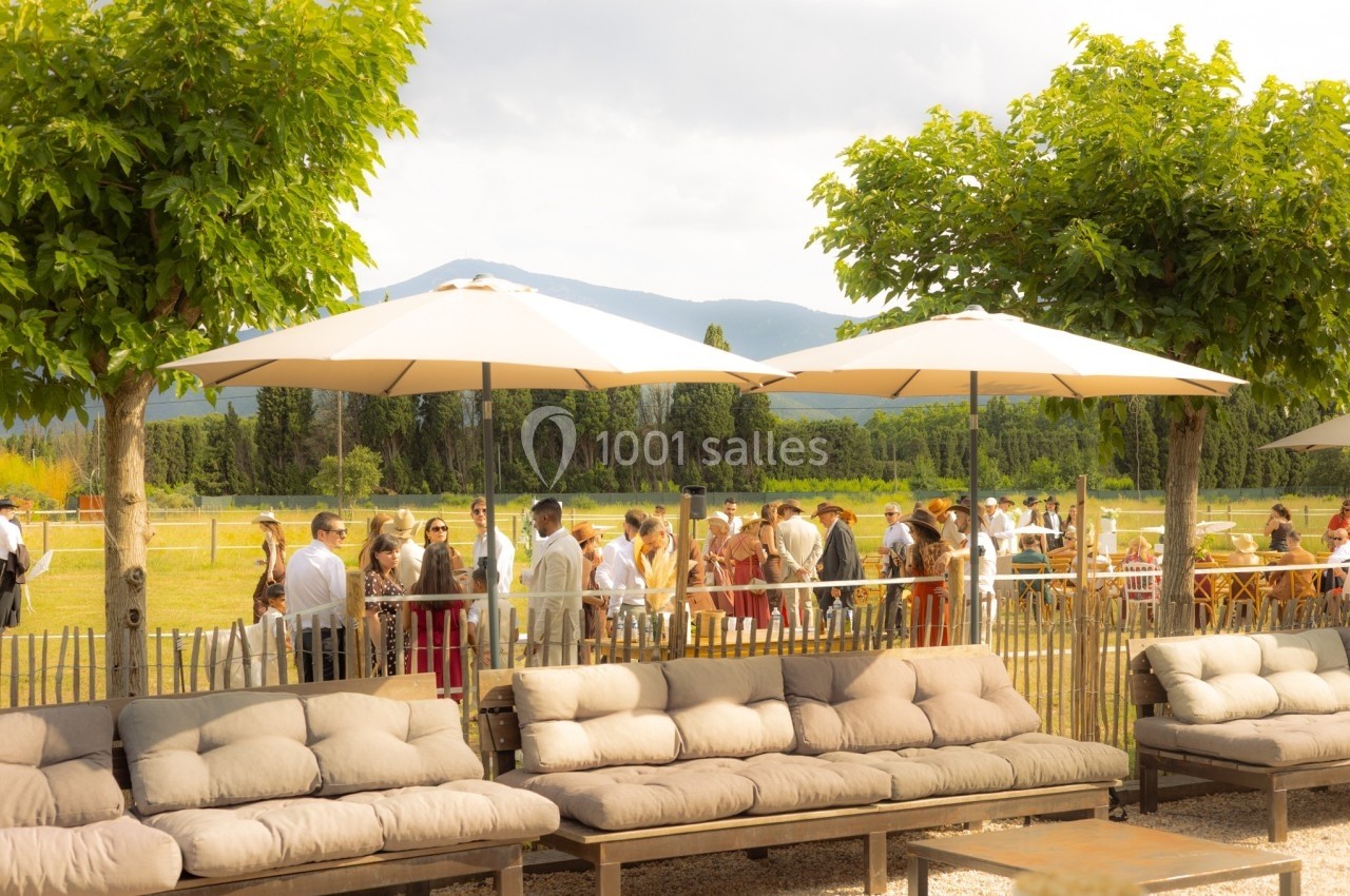 Groupe de personnes rassemblées dans un jardin ensoleillé, avec des parasols et des canapés à l'avant-plan.