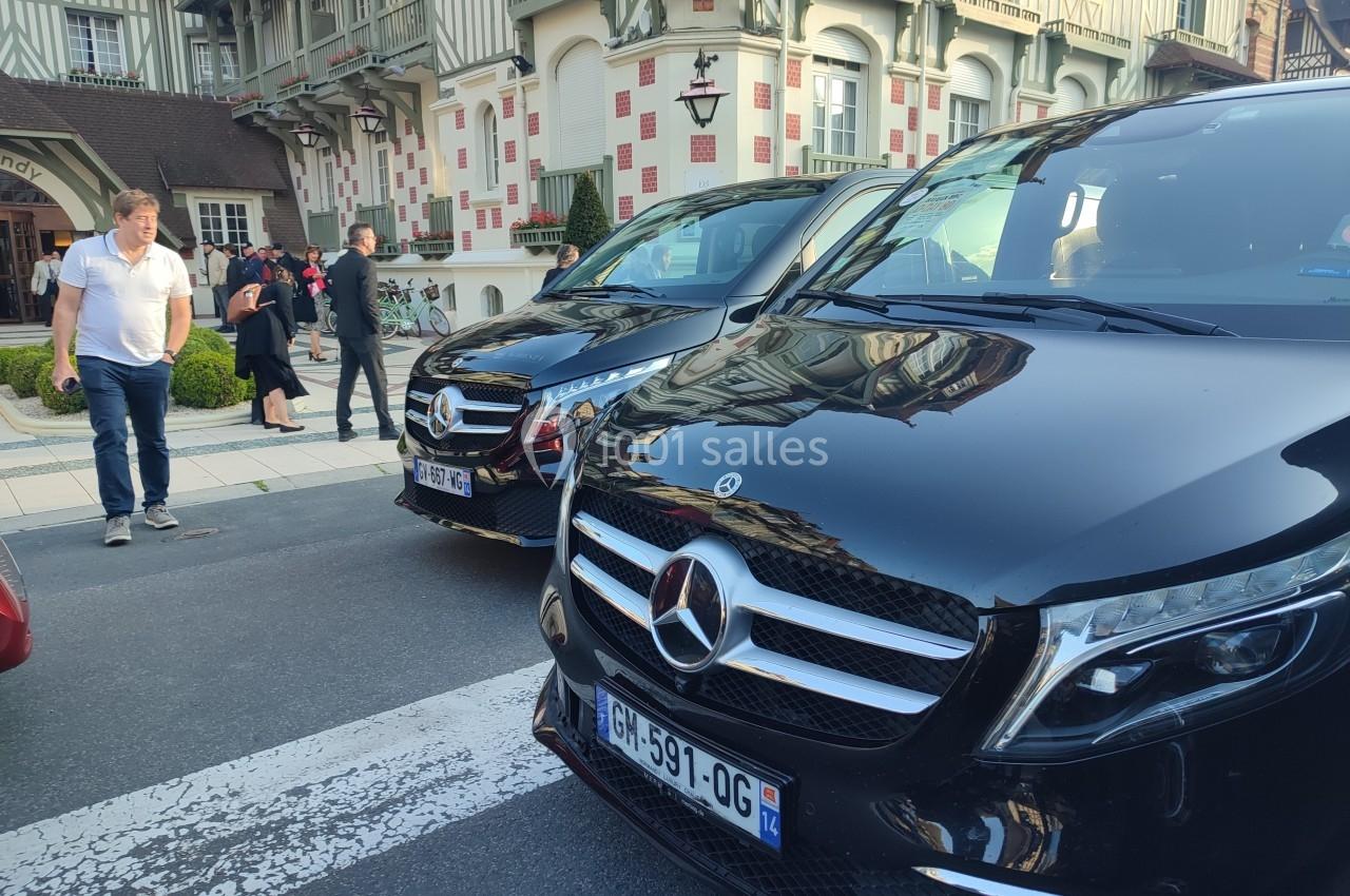 Deux vans noirs Mercedes garés sur une rue près d'un bâtiment à colombages, avec des passants en arrière-plan.