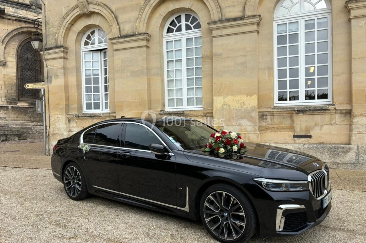 Voiture noire décorée de fleurs rouges et blanches, stationnée devant un bâtiment en pierre avec grandes fenêtres.