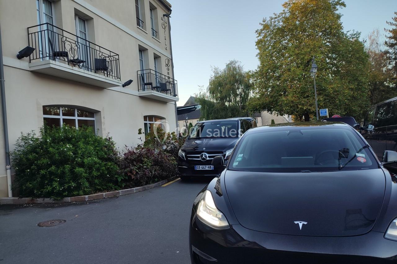 Voiture noire garée devant un bâtiment beige à plusieurs étages, entouré de végétation et d'autres véhicules.