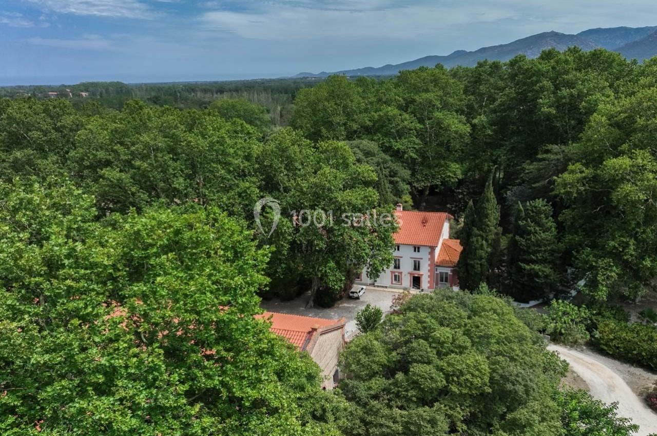 Vue aérienne d'une maison avec toit en tuiles rouges entourée de forêt dense, au pied de collines.