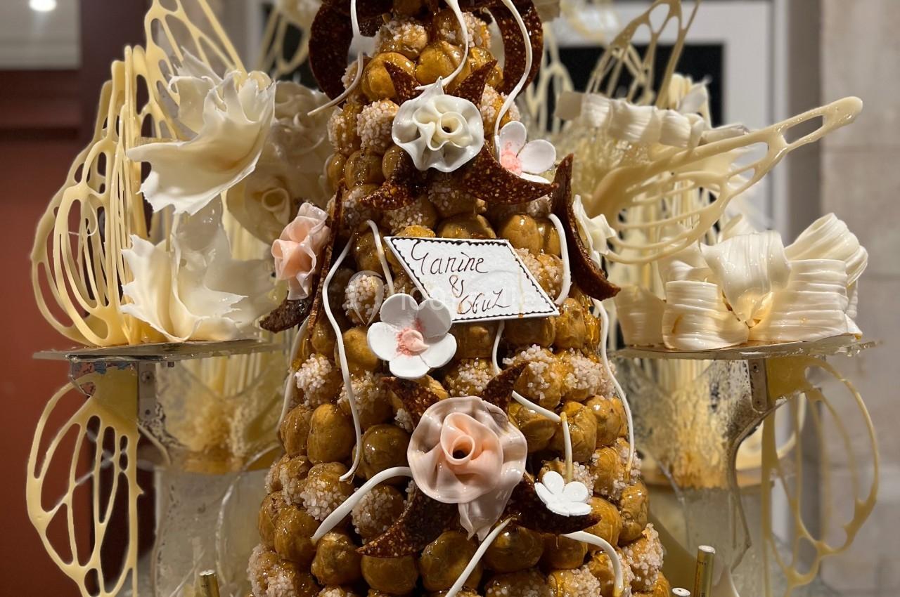 Pièce montée en choux décorée de fleurs en sucre, avec figurines de mariage au sommet et détails en caramel filé.