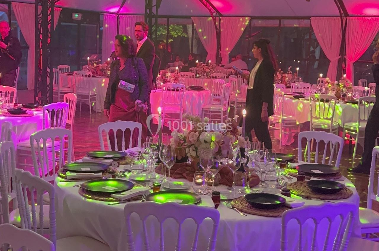 Salle de réception décorée avec des tables dressées, des chandeliers suspendus et un éclairage coloré.