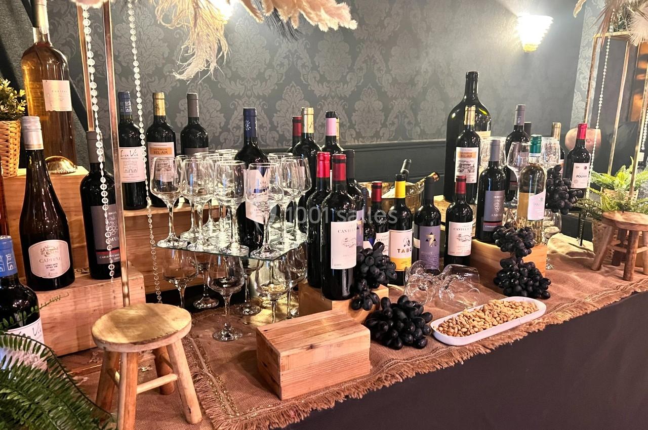 Table garnie de bouteilles de vin, verres, raisins noirs et noix, décorée avec des éléments naturels et boisés.