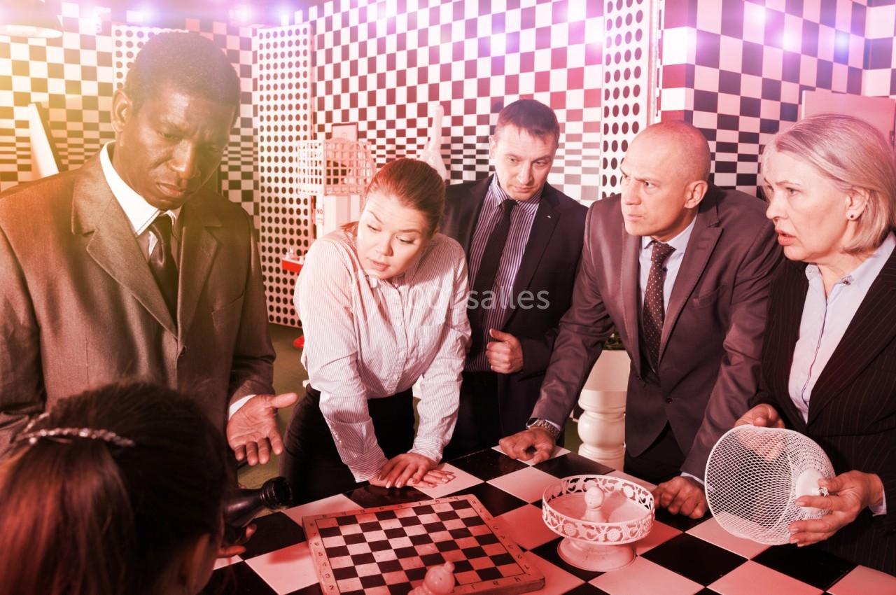 Des personnes en tenue professionnelle discutent autour d'une table avec un échiquier et divers objets.