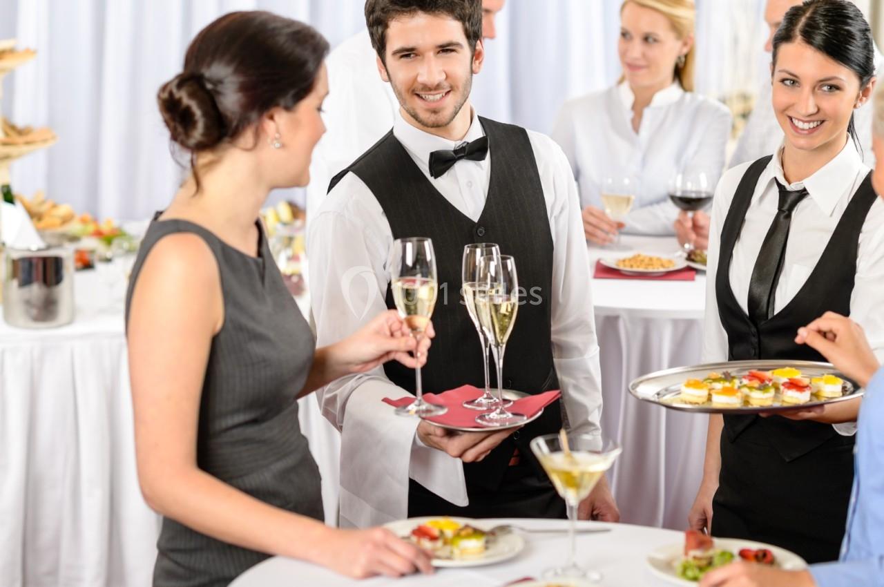 Serveur en tenue formelle servant des boissons lors d'un événement avec des invités debout autour de tables.