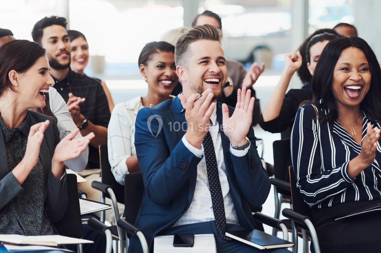 Des personnes assises dans une salle applaudissent et sourient, semblant assister à une présentation ou un événement.